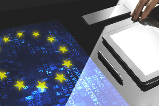 refer to: Responsibilities of the Single Contact Point (ZASt) (Source: ©denizbayram - stock.adobe.com) there is a tablet and pen in front of a screen with the EU flag (refer to: Responsibilities of the Single Contact Point (ZASt))